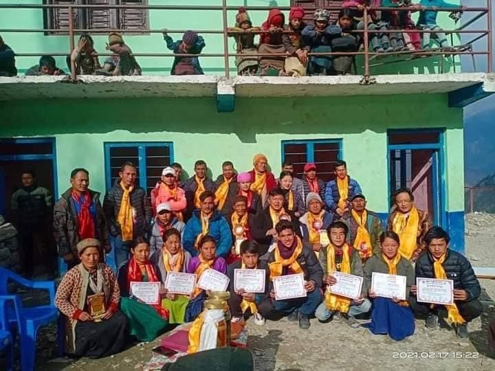 Scholarship recipients holding their certificates, with families and community members behind them